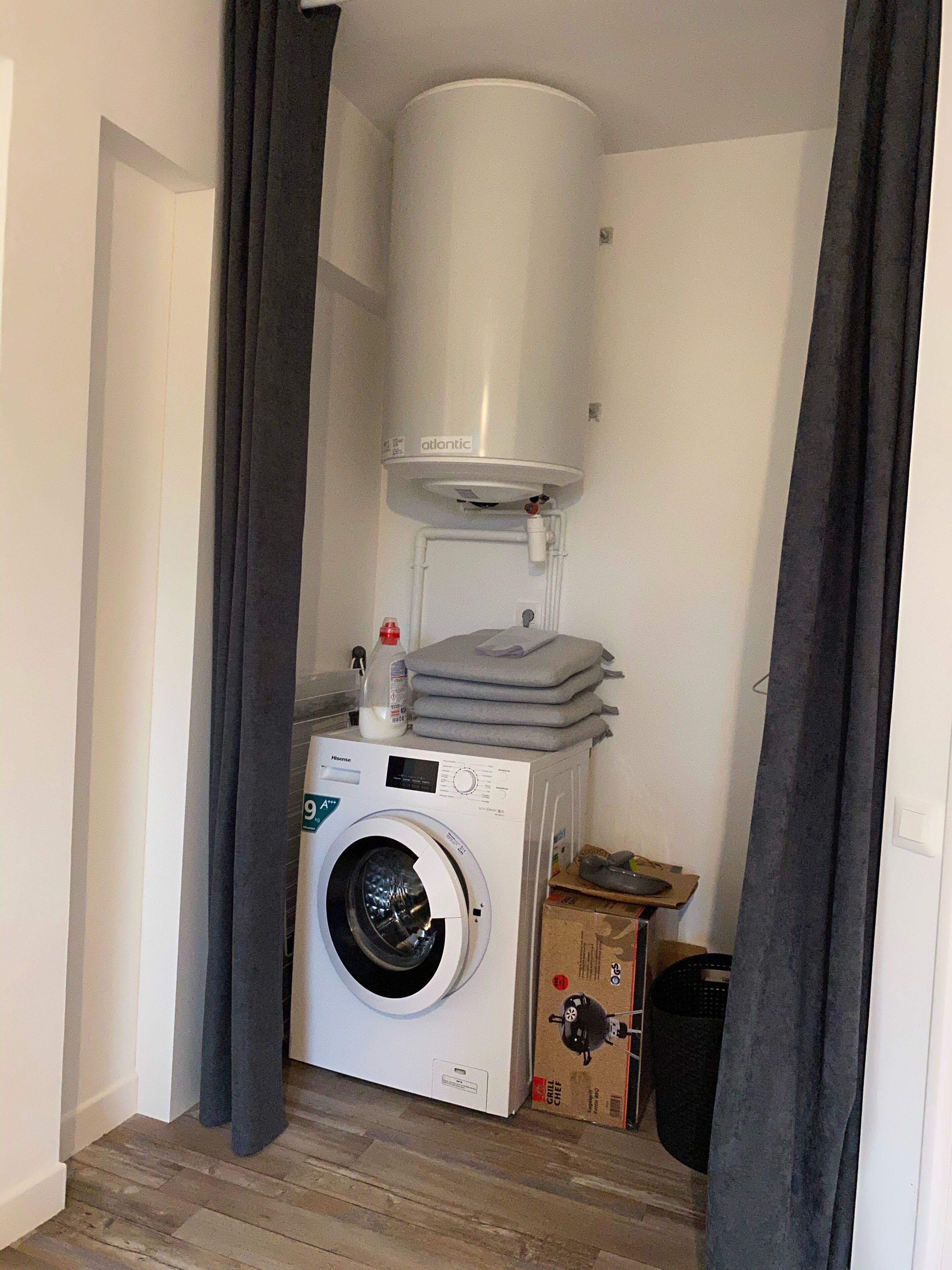 A compact laundry room with a front-loading washing machine, a stacked drying rack, and a water heater.