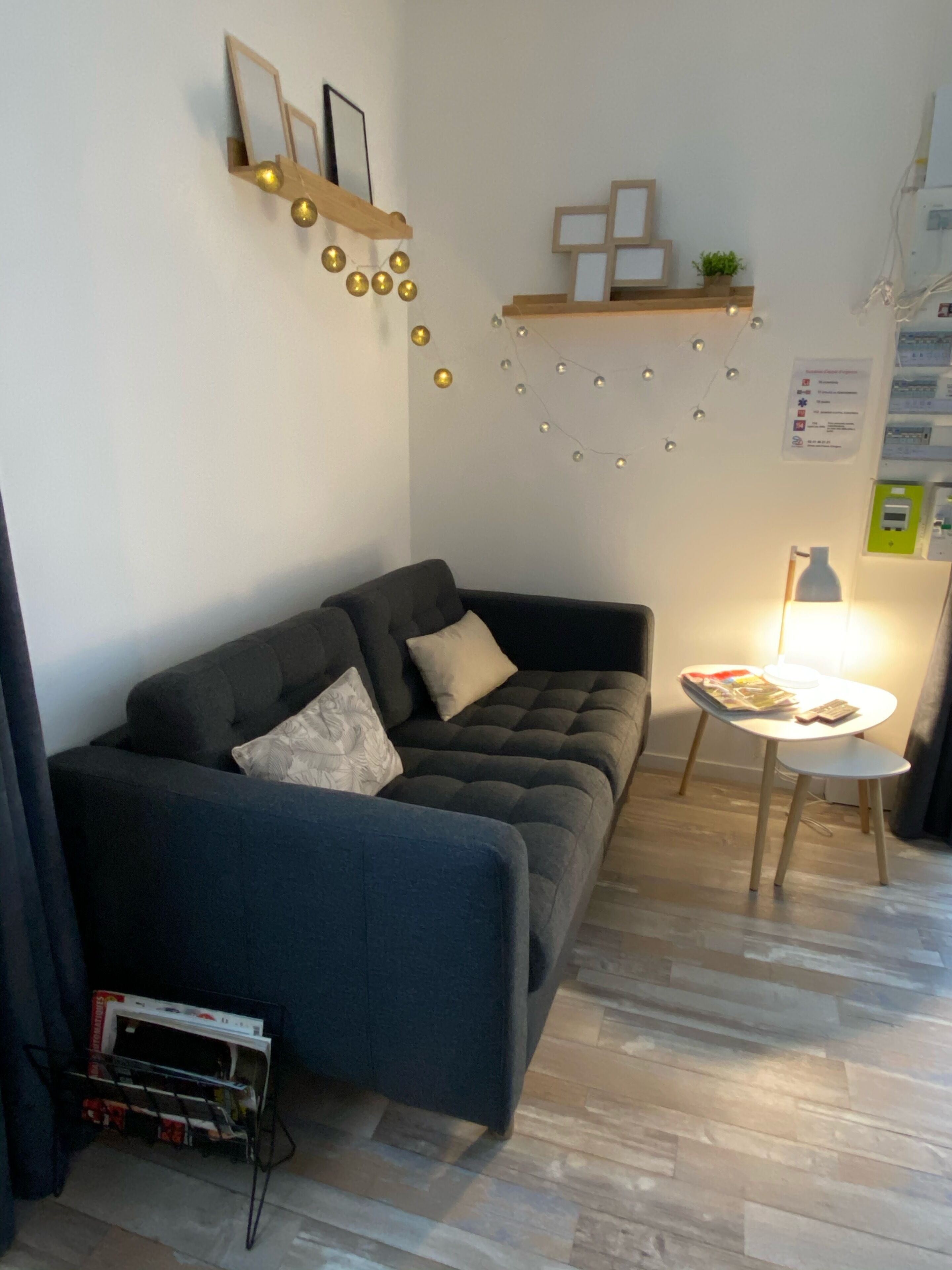 Una sala de estar moderna con un sofá gris oscuro, una mesita redonda con una lámpara y un estante de madera con adornos.