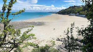 A beach with clear blue water, sandy shore, and rocky areas. There are trees in the foreground and a hill with buildings in the background. - Appartements Résidence des 3 îles - Binic-Etables sur mer (Binic-Etables-sur-Mer)