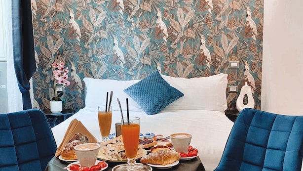 Una habitación de hotel con una cama, una mesa servida con desayuno y un papel tapiz floral.