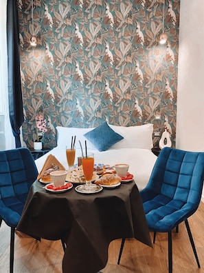 Una habitación de hotel con una cama, una mesa servida con desayuno y un papel tapiz floral.