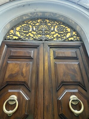 Puerta doble de madera con detalles metálicos ornamentales y dos aldabillas de latón.