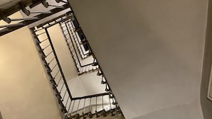 Una escalera con barandilla metálica, un accesorio de iluminación en la pared y una puerta al final.