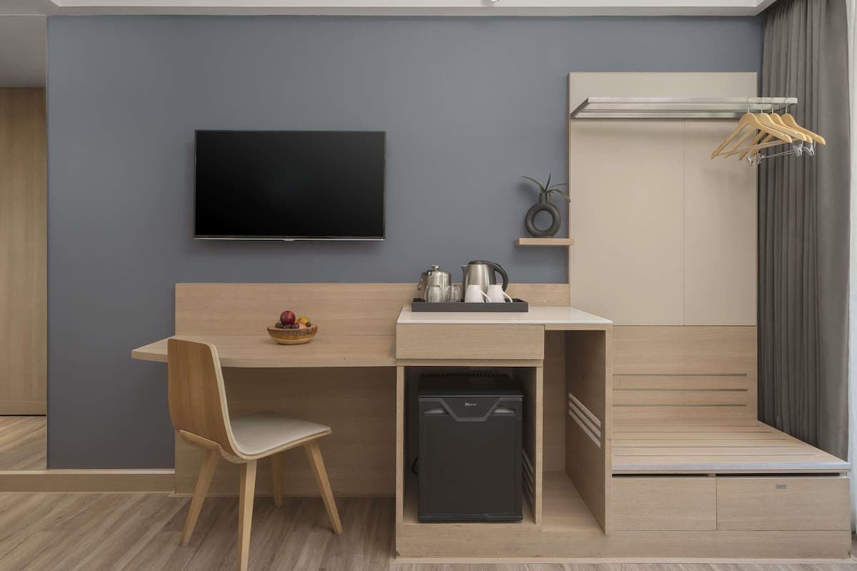 Una habitación moderna y funcional con televisión de pantalla plana, un escritorio de madera con silla, un refrigerador pequeño y un armario empotrado.