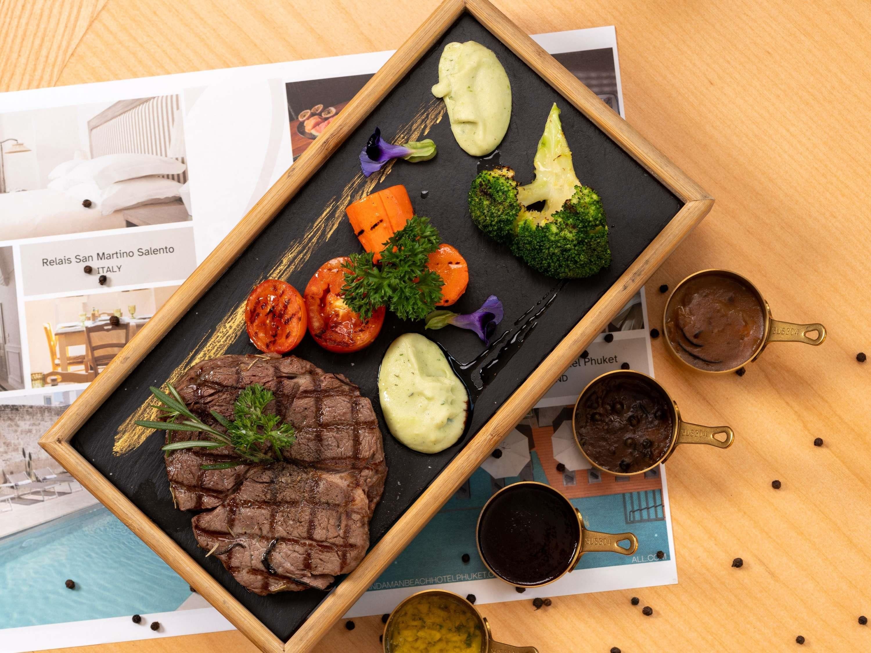 A meal with steak, vegetables, and sauces on a black slate.