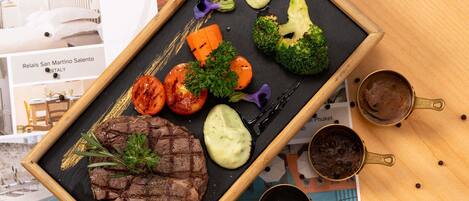 A meal with steak, vegetables, and sauces on a black slate.