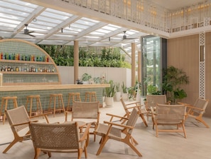 A bar area with wicker chairs and a bar counter, surrounded by potted plants and a glass enclosure. - Andaman Beach Hotel Phuket - Handwritten Collection by Accor (Patong)