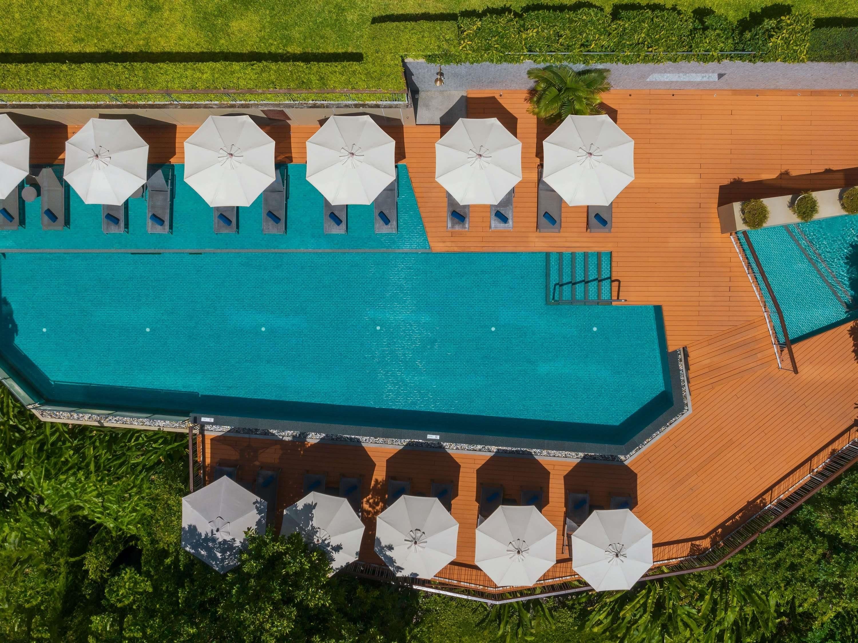 Vista aérea de un hotel con una gran piscina, múltiples sombrillas y una zona de terraza de madera.