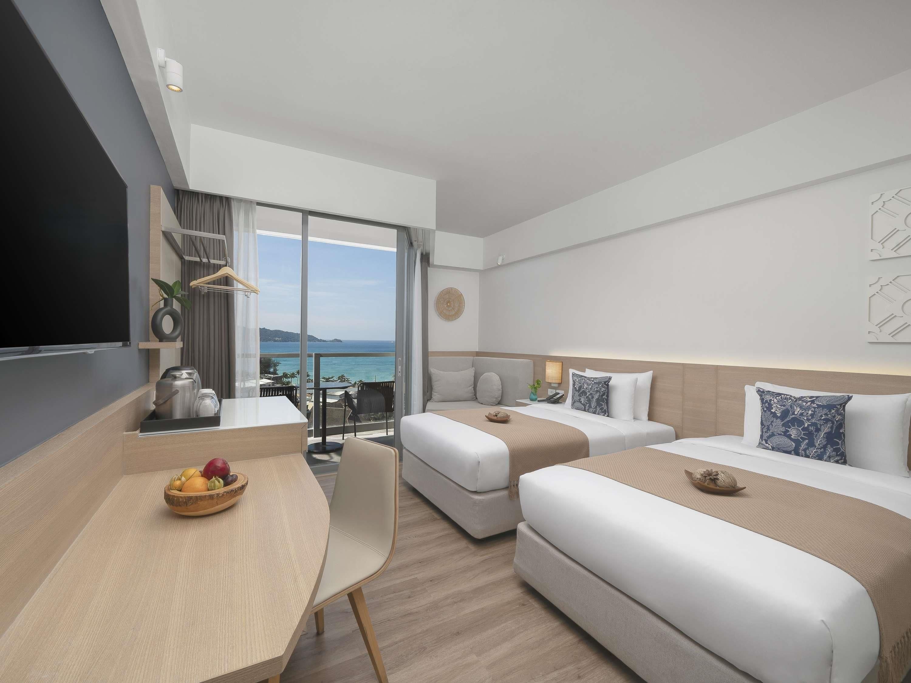A modern hotel room with a balcony, a dining area, and a bed with a view of the sea.