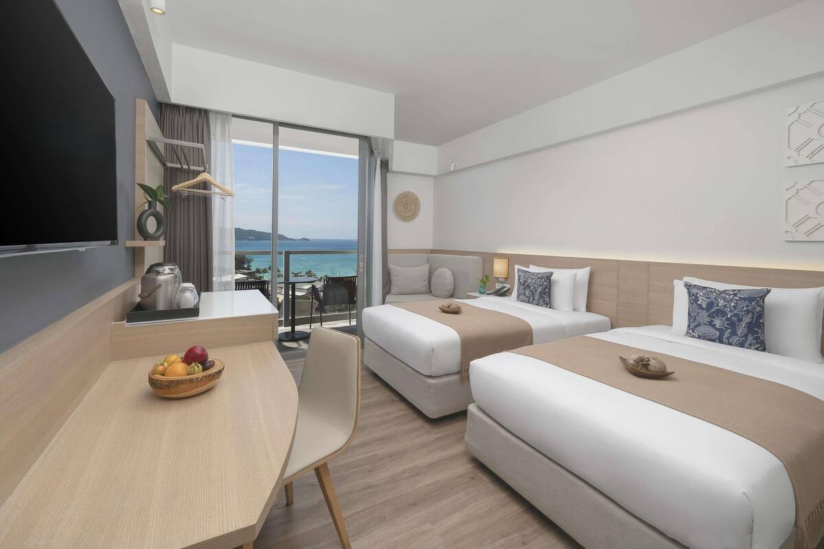 A modern hotel room with a balcony, a dining area, and a bed with a view of the sea.