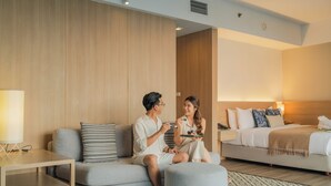 A modern hotel room with a sofa, ottoman, bedside table, and a bed with pillows and a blanket. - Andaman Beach Hotel Phuket - Handwritten Collection by Accor (Patong)