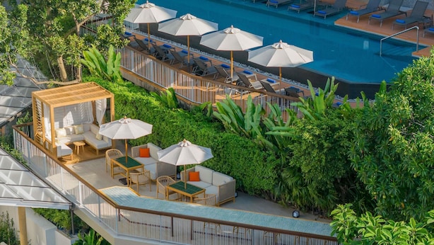 A rooftop pool area with lounge chairs, umbrellas, and a seating area with sofas and tables.