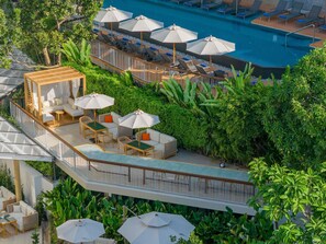 Un área de piscina en la azotea con sillones de descanso, sombrillas y un espacio de estar con sofás y mesas.