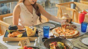 A dining table with a variety of dishes, including a pizza, salad, and a burger. - Andaman Beach Hotel Phuket - Handwritten Collection by Accor (Patong)