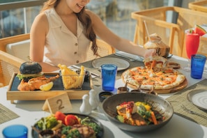 A dining table with a variety of dishes, including a pizza, salad, and a burger. - Andaman Beach Hotel Phuket - Handwritten Collection by Accor (Patong)