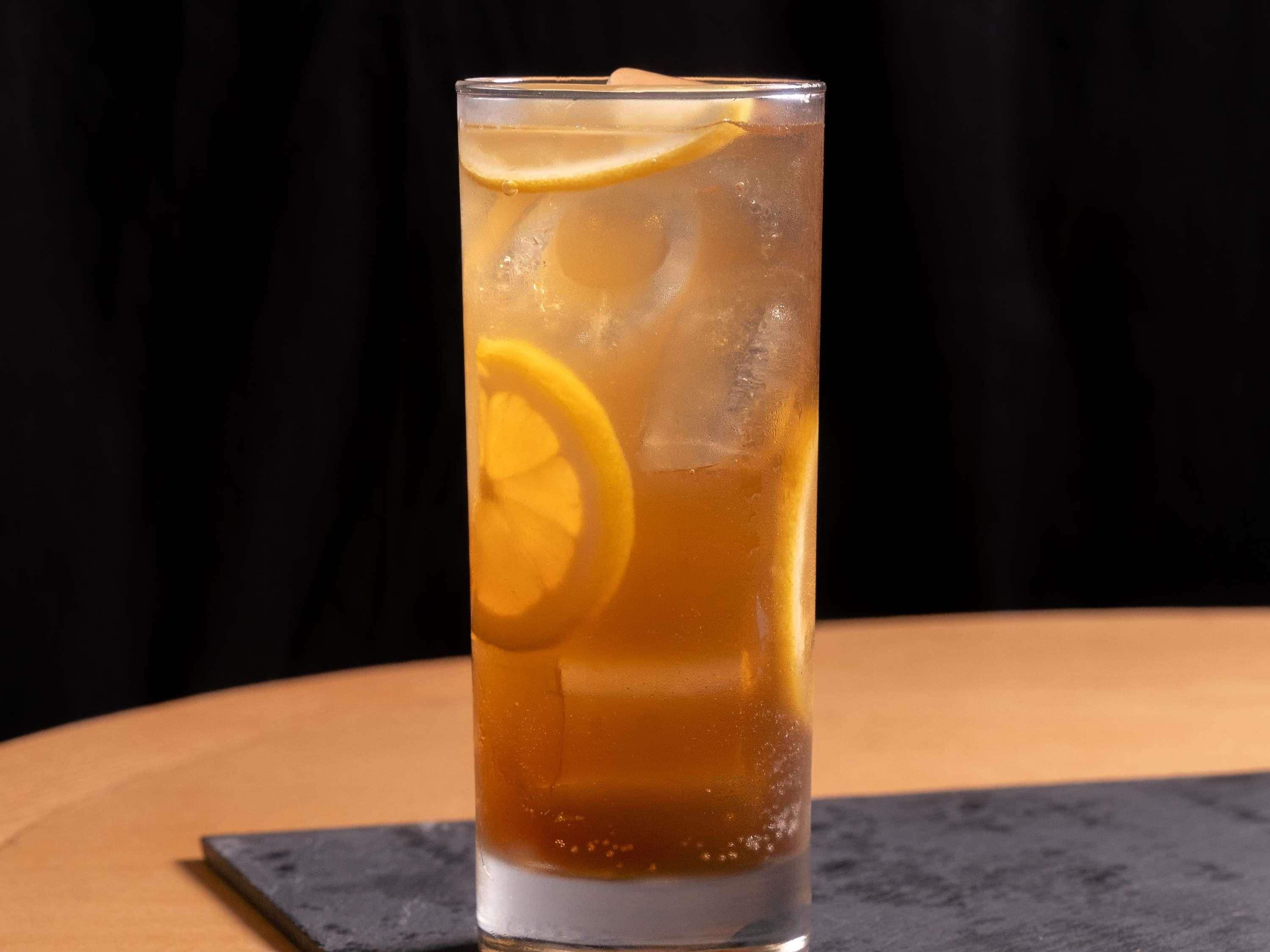 A tall glass with a beverage, ice cubes, and a lemon slice.
