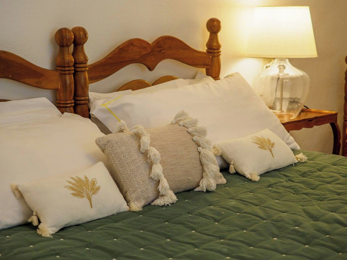 A bed with a wooden headboard, multiple pillows, a green quilt, and a bedside lamp.