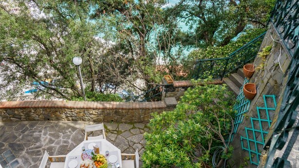 An outdoor dining area with a stone patio, a table set for four, surrounded by greenery and a stone wall. - Villa Tanca with Terrace and Views (Monterosso al Mare)