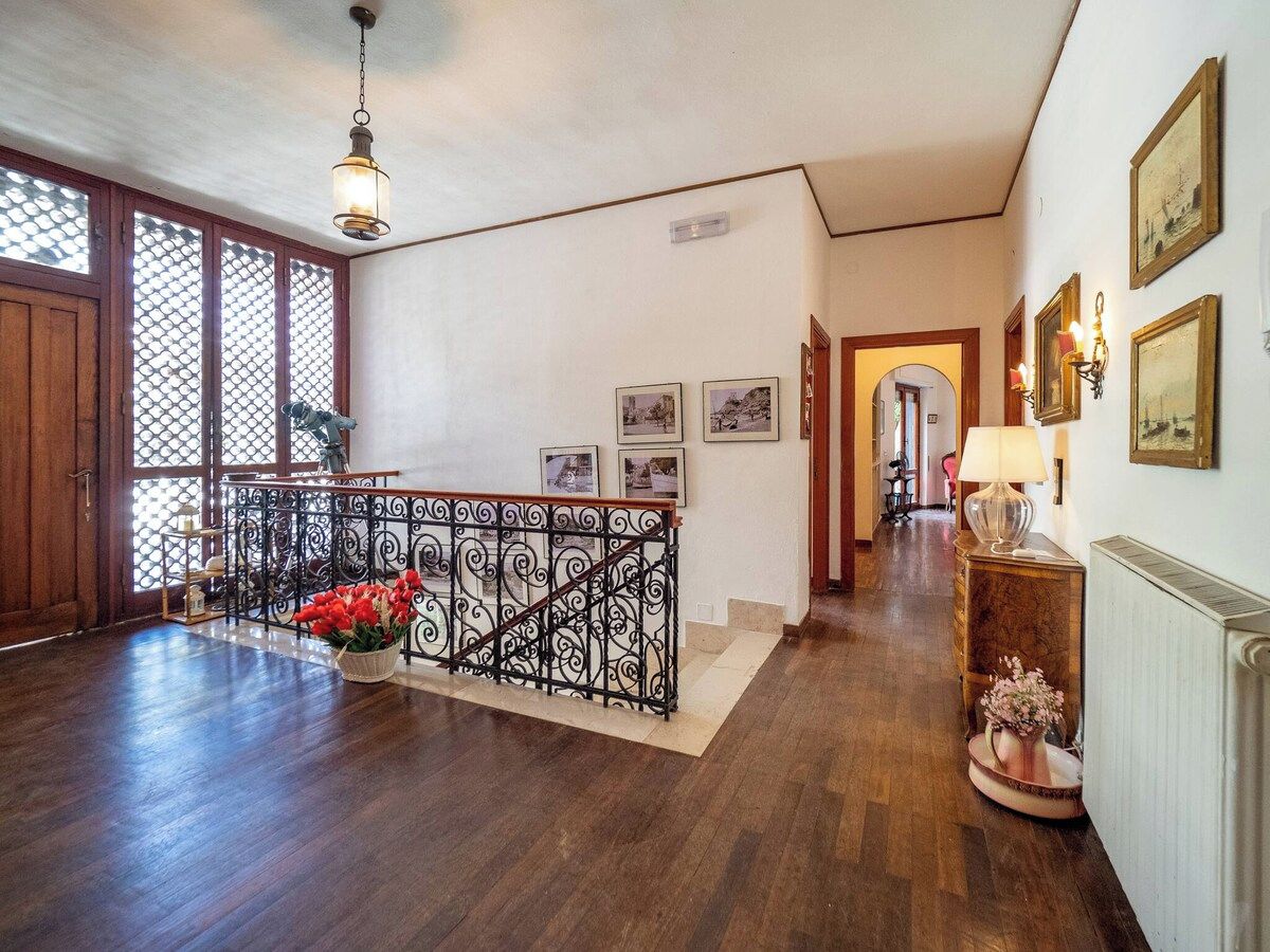 A spacious hallway with wooden flooring, a decorative railing, and a potted plant.