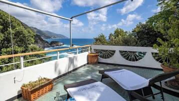 A rooftop terrace with a view of the sea, lounge chairs, and a small table with a bottle.