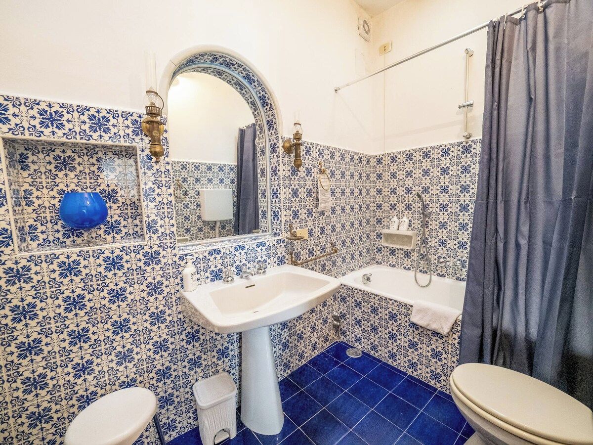 A bathroom with a white sink, a mirror, a blue-tiled floor, and a shower area.
