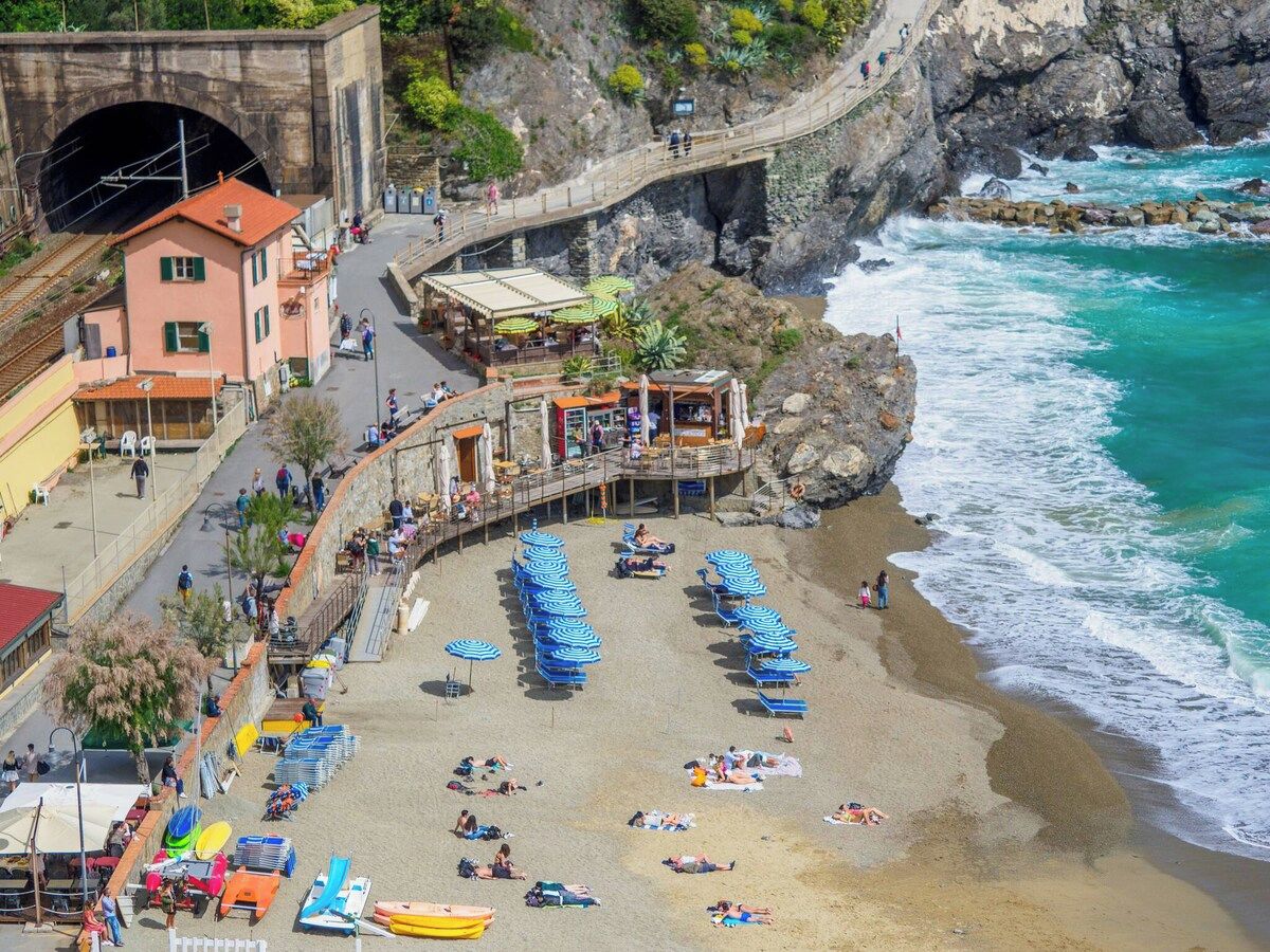 Une ville côtière avec une plage, un pont en pierre et un bâtiment doté d’un toit rouge.