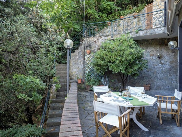 An outdoor dining area with a stone wall, a staircase, and a small tree.