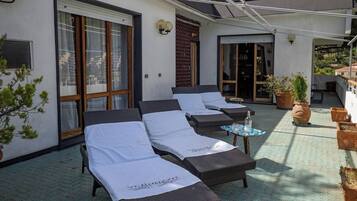 A sunlit outdoor lounge area with multiple seating options, including lounge chairs and a small table, surrounded by potted plants.