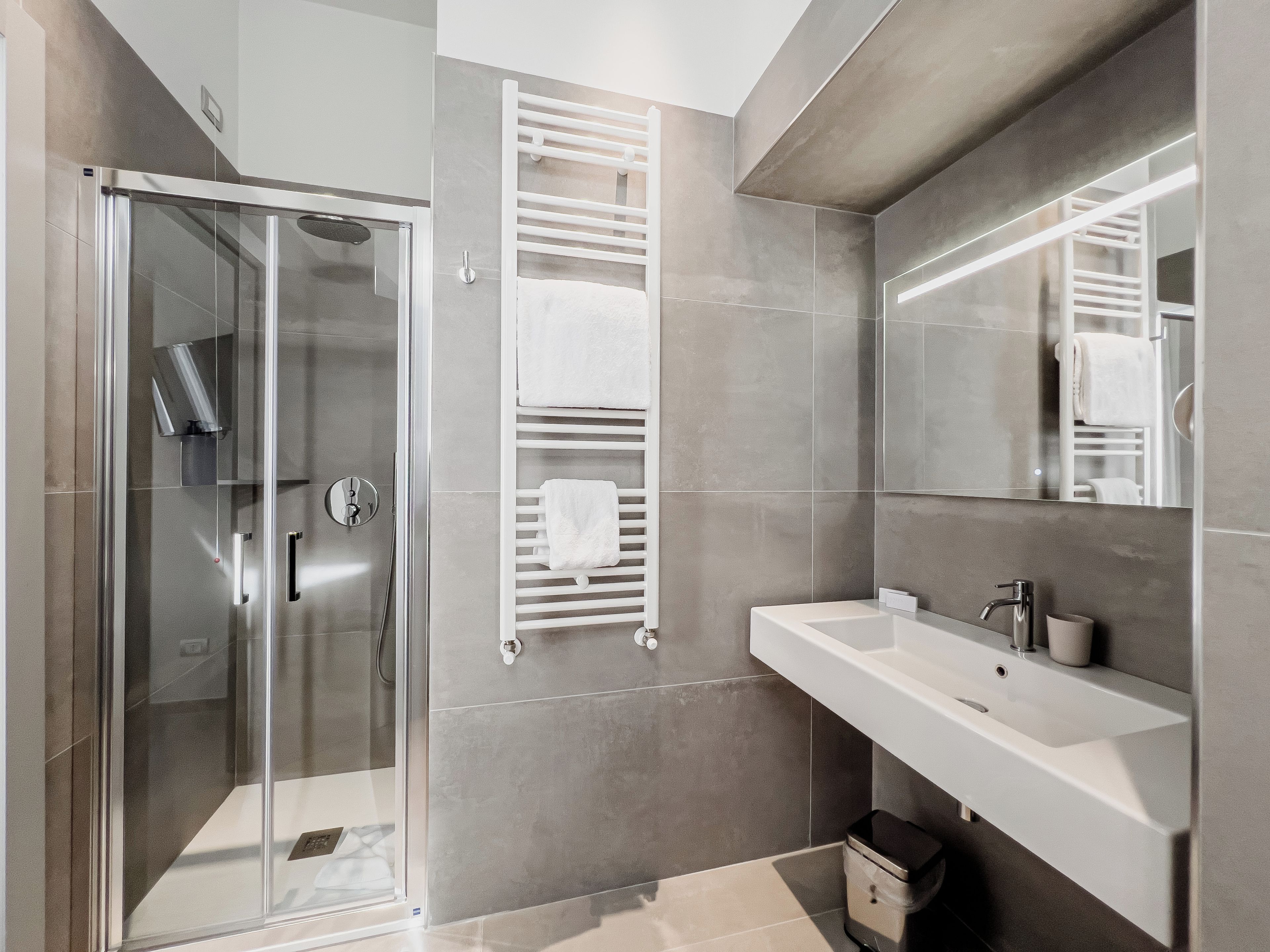 Un bagno moderno con cabina doccia in vetro, lavandino bianco e uno specchio grande.