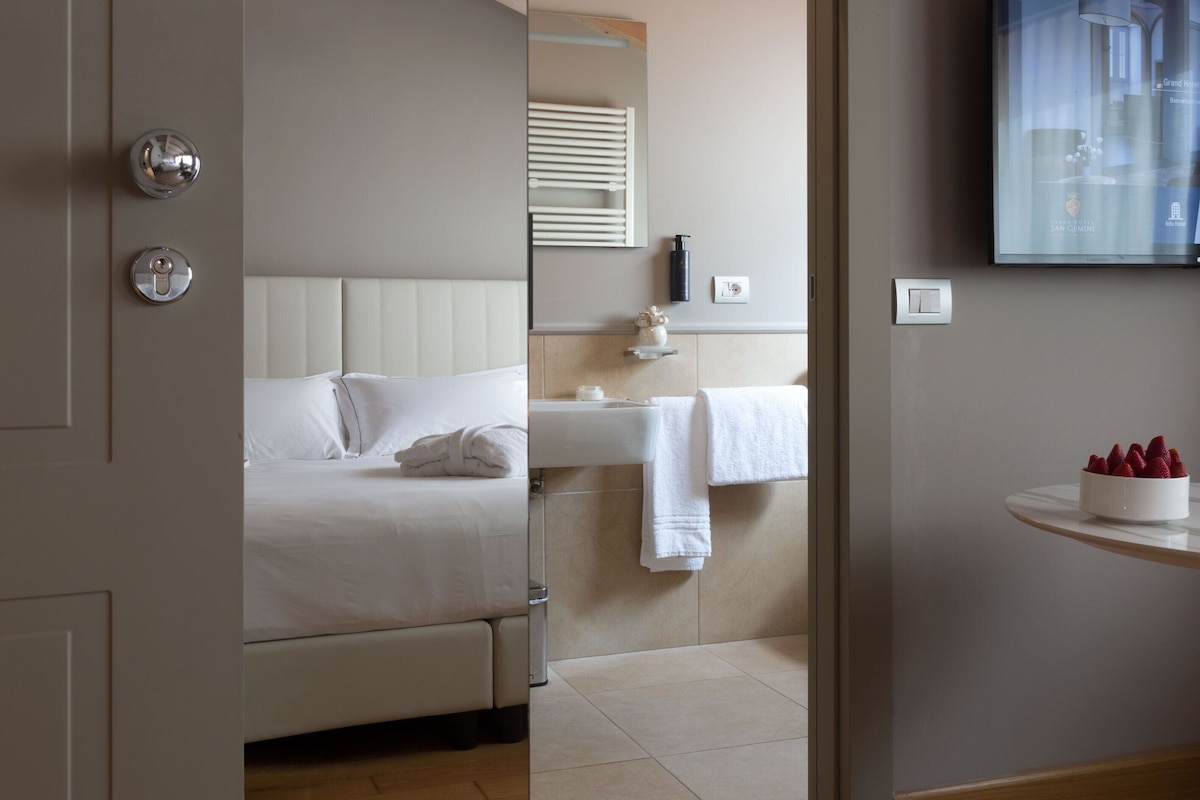 A hotel room with a bed, a bathroom with a sink and mirror, and a wall-mounted TV.