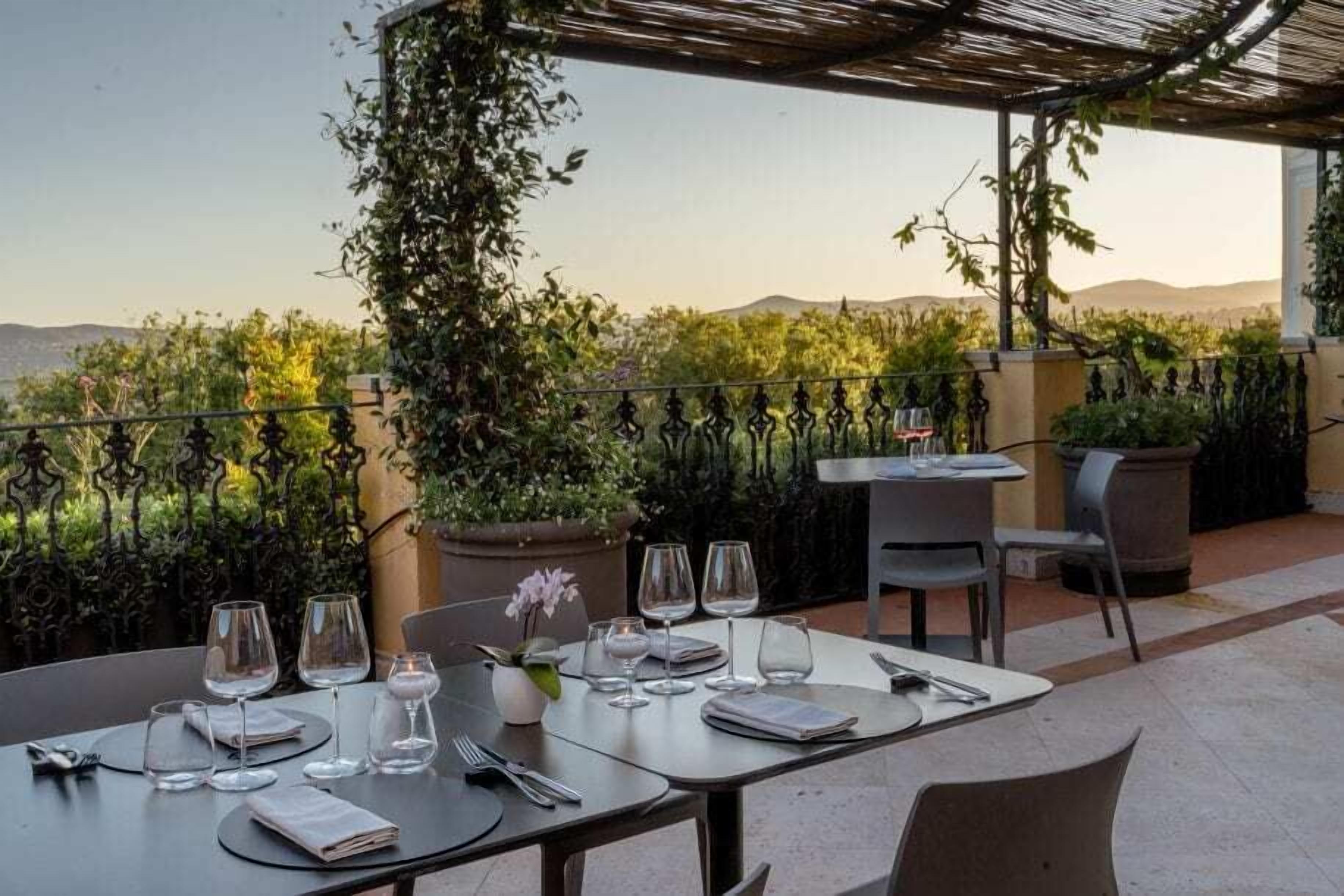 Une terrasse avec des tables dressées pour le dîner, offrant une vue sur un paysage montagneux.