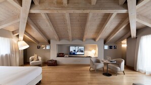 A spacious room with a high ceiling, wooden beams, a bed, two armchairs, a small table with a laptop, and a television on the wall. - Grand Hotel San Gemini | UNA Esperienze. (San Gemini)
