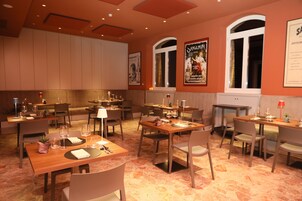 Un restaurante con varias mesas y sillas, dispuesto en un espacio amplio con techos altos y ventanas grandes.