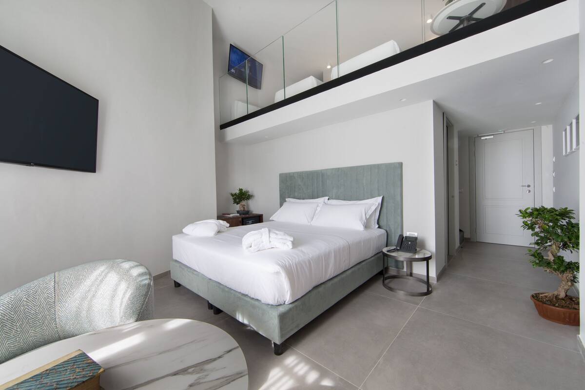 Un dormitorio moderno con una cama grande, una mesita de noche, una silla y una planta en maceta.