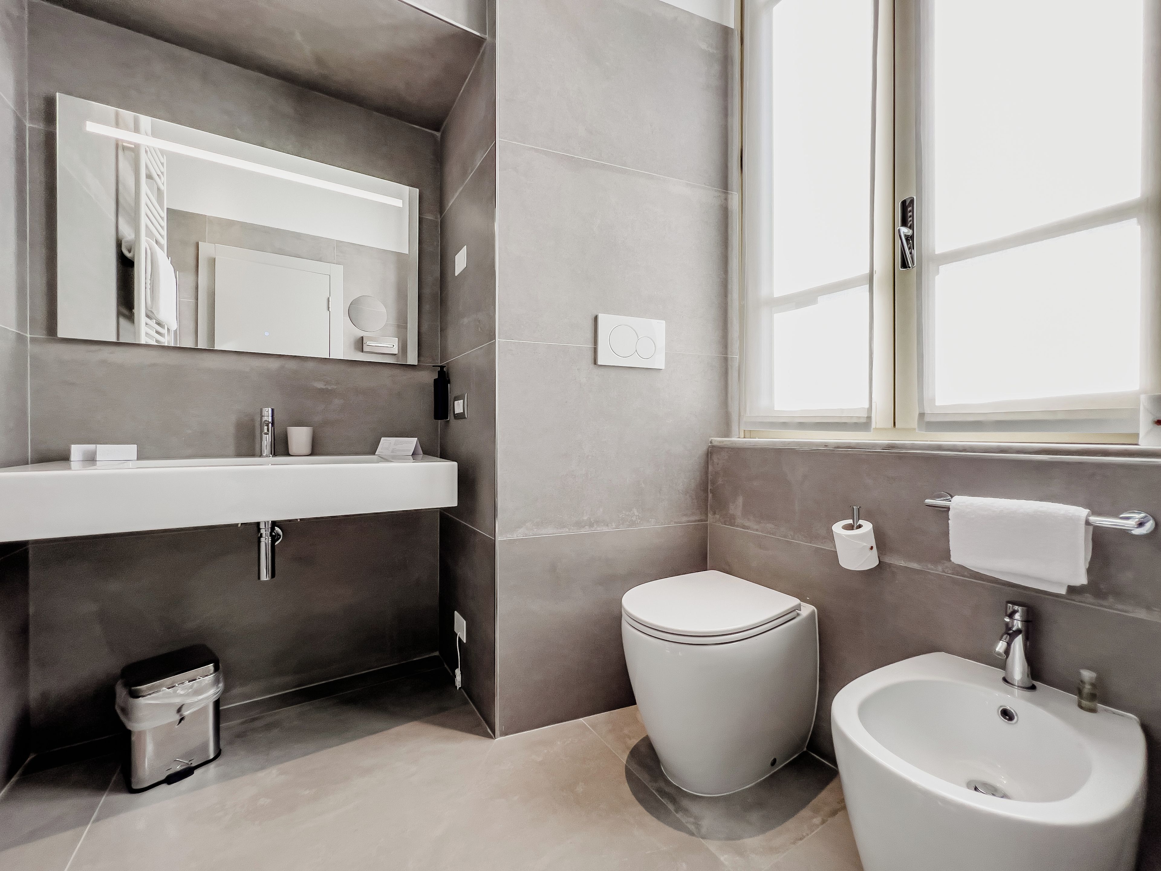 A modern bathroom with a vanity, toilet, bidet, and a window.