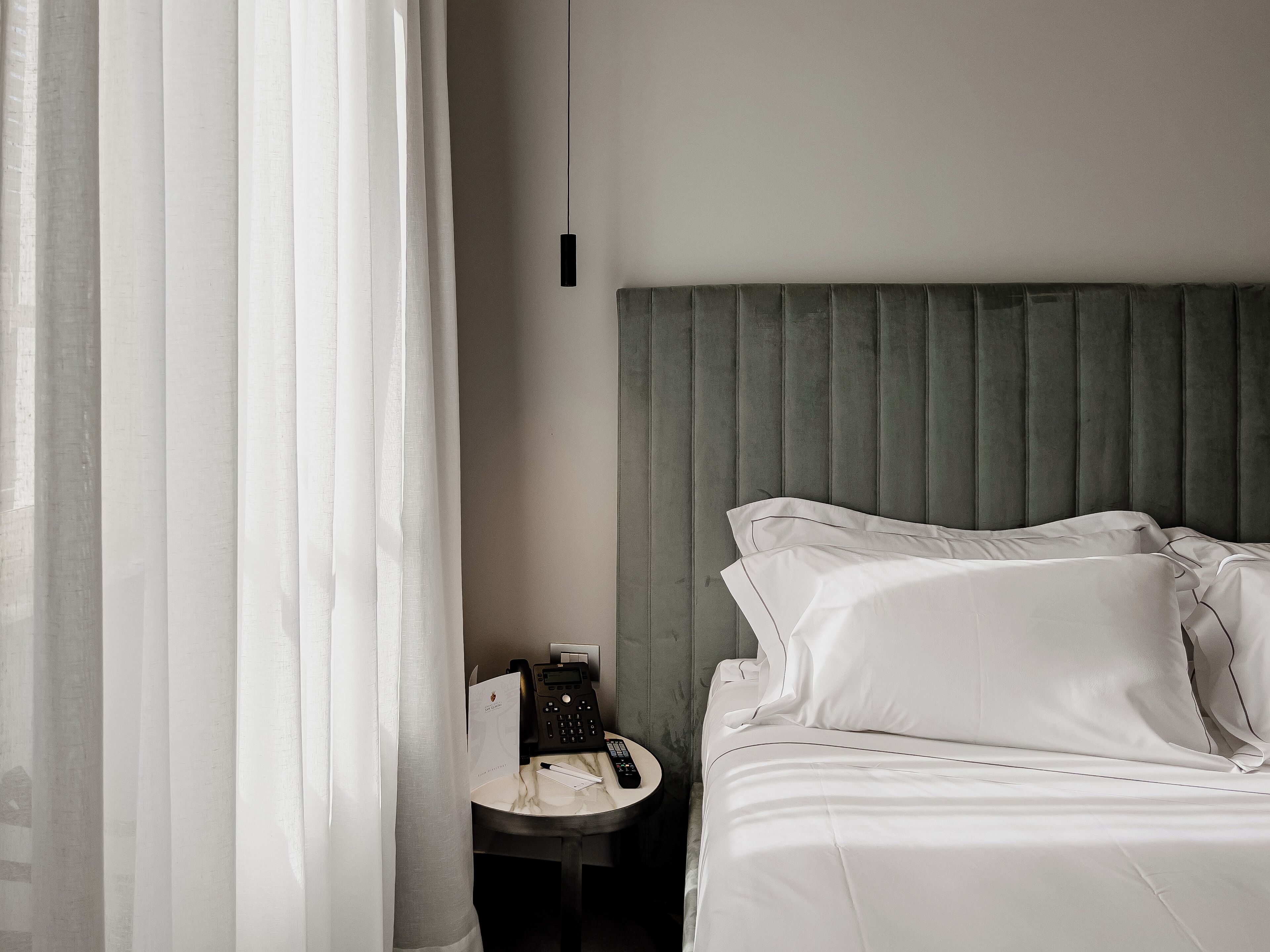A hotel room with a bed, a nightstand, a telephone, and a curtain.