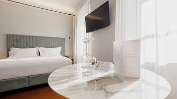 A hotel room with a bed, a round marble table, a TV mounted on the wall, and a window with curtains.