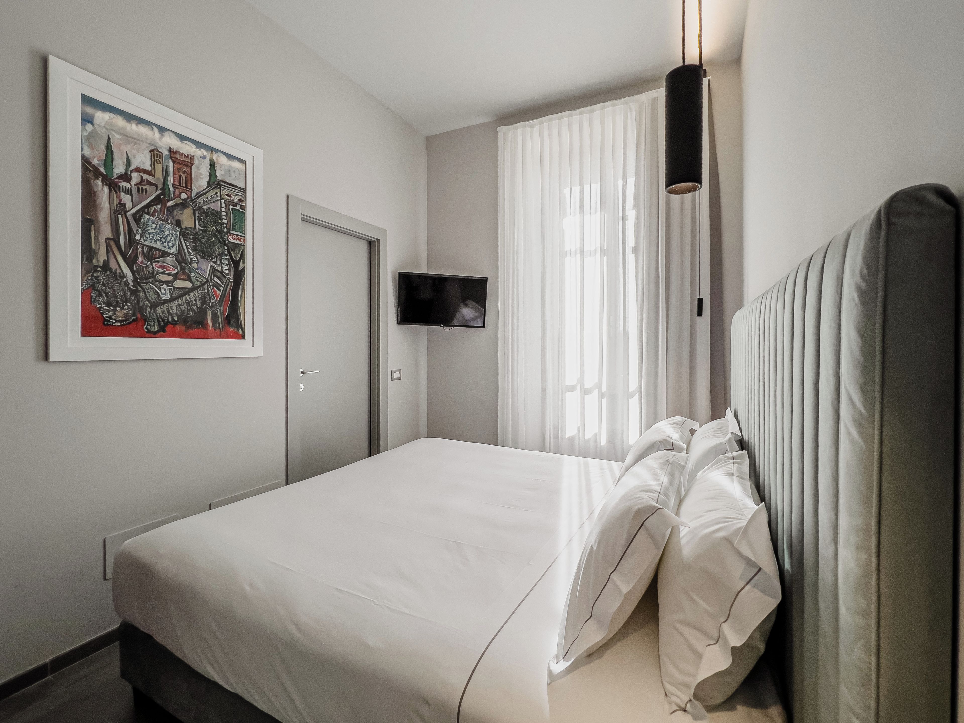 Une chambre d’hôtel avec un lit, une télévision, un tableau et une fenêtre avec des rideaux.