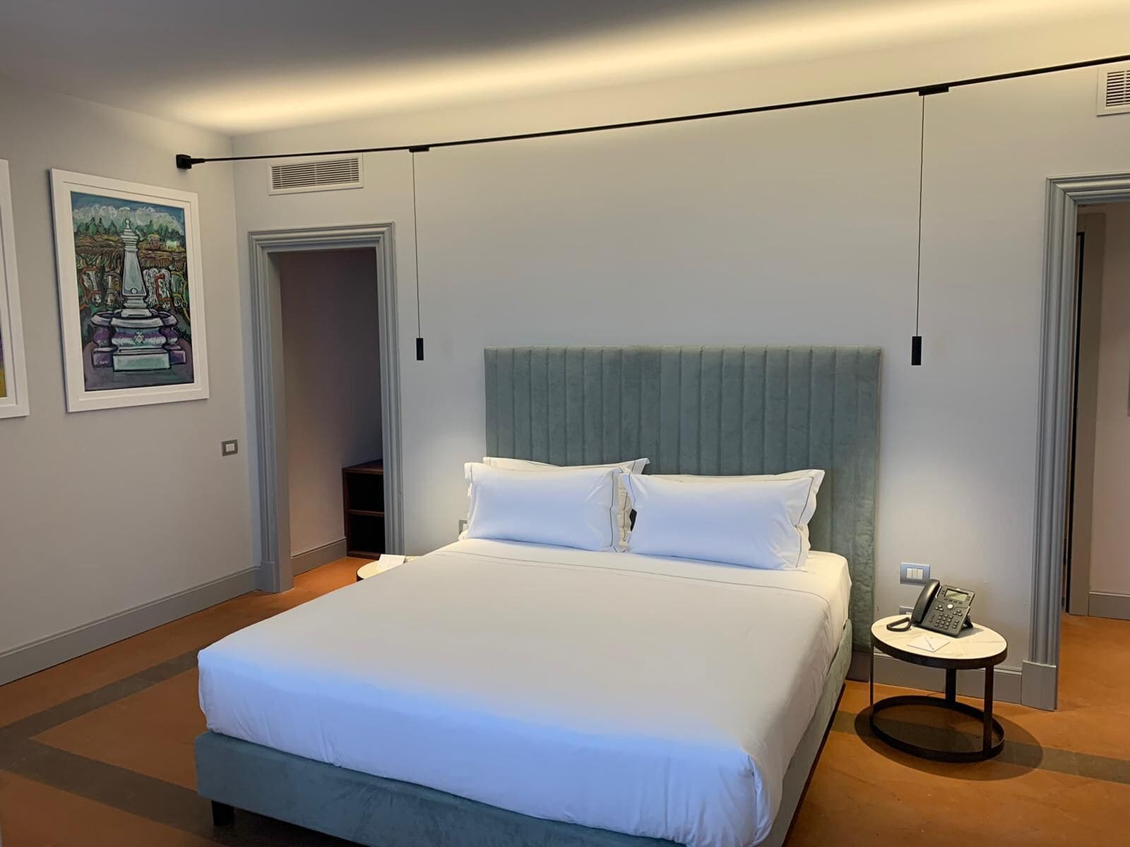 Una habitación de hotel moderna con una cama grande, una mesita de noche con un teléfono y un cuadro en la pared.