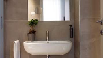 Un baño moderno con lavamanos blanco, un espejo, una planta en maceta, una toalla y un cubo de basura.