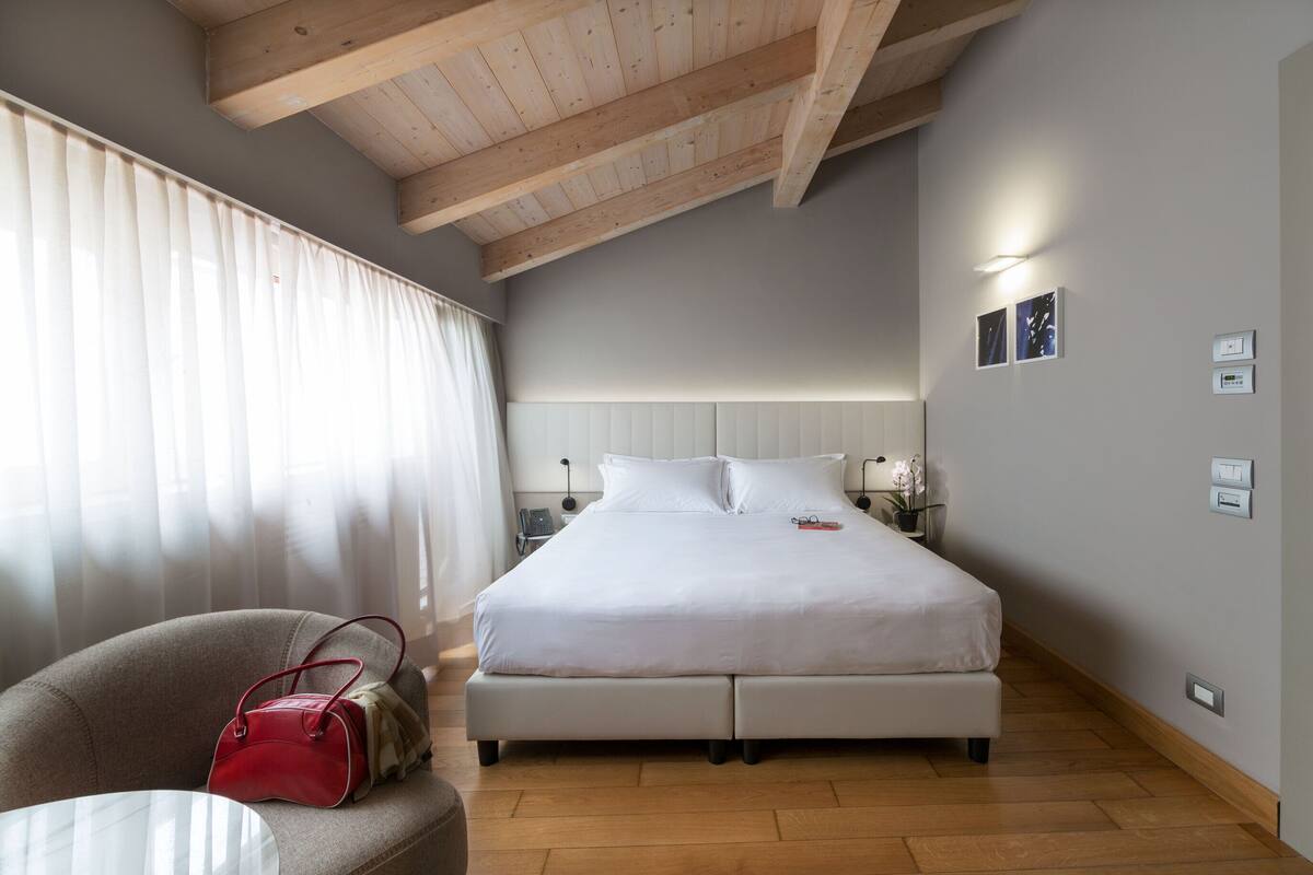 Un dormitorio con una cama, una silla, una mesa y un bolso rojo.