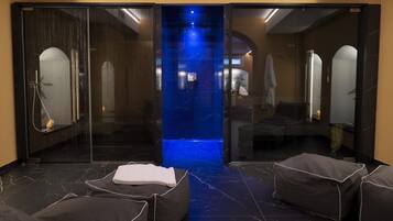 Un espace de détente moderne avec une paroi en verre, une fontaine illuminée de couleur bleue et des coins salon confortables.