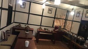 A room with wooden flooring, a sofa, a dining table, and a long counter with multiple light fixtures. - OurGuest Camp Lachung (Chungthang)