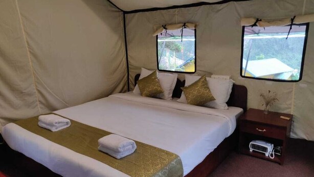 A tent-style room with a bed, two windows, a bedside table, and a small shelf. - OurGuest Camp Lachung (Chungthang)