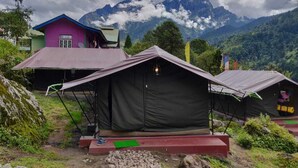 A mountain lodge with tents and a colorful building, surrounded by lush greenery and mountains. - OurGuest Camp Lachung (Chungthang)