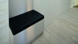 Um corredor com paredes brancas, um banco preto e uma porta no final.