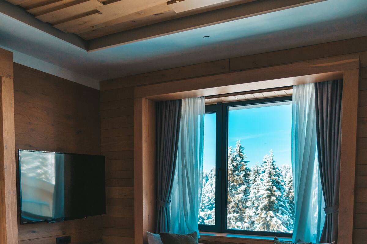 A bedroom with a large bed, a flat-screen TV mounted on the wall, and a window with curtains.