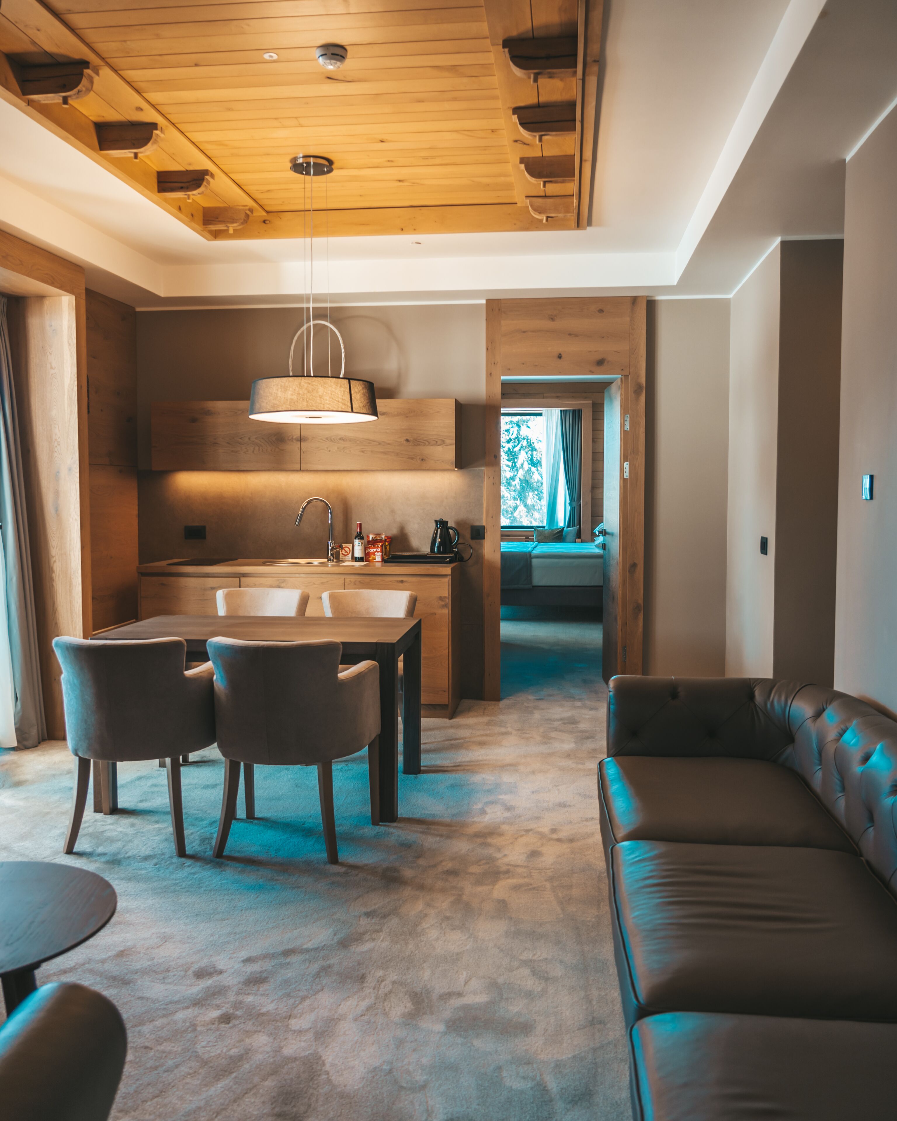 A modern interior with a wooden ceiling, a dining area with a table and chairs, a sofa, and a kitchen area with a sink and cabinets.