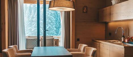 A modern kitchen with wooden cabinets, a dining area with a table and chairs, and a large window with curtains.