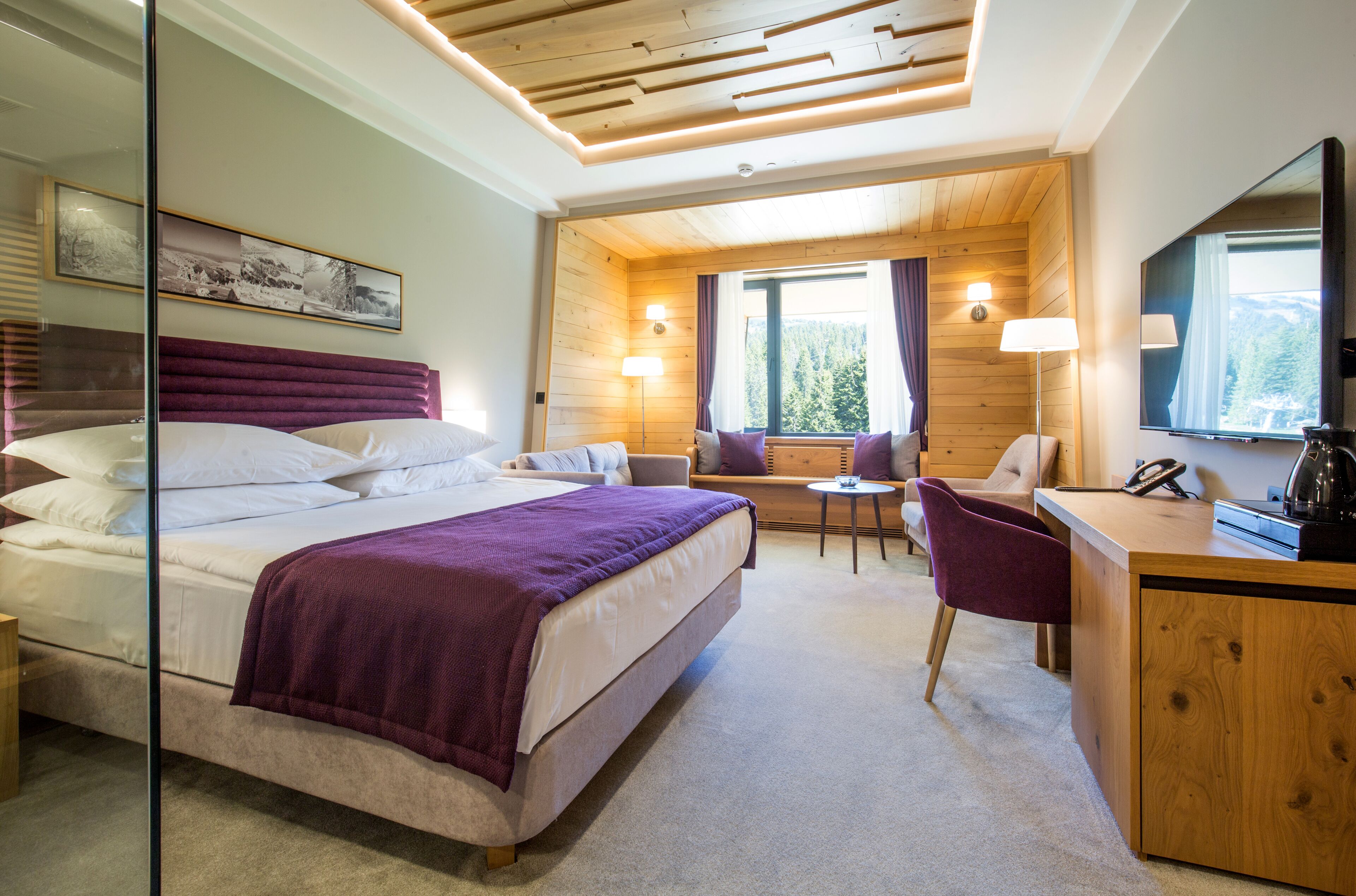 Een slaapkamer met een bed, een bureau, een stoel, een klein tafeltje en een raam met gordijnen.